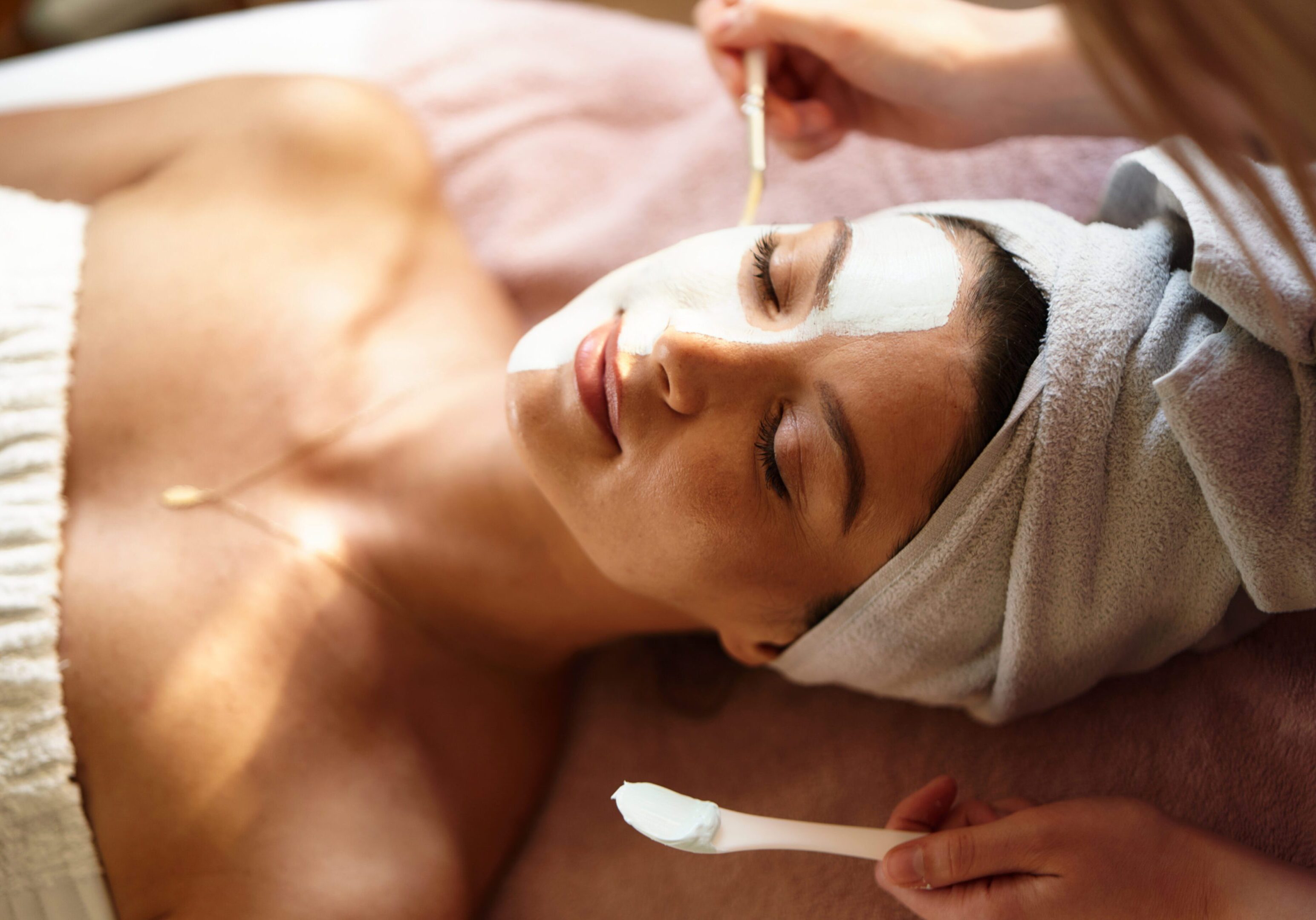Client lies as the beautician applies cream to her face.